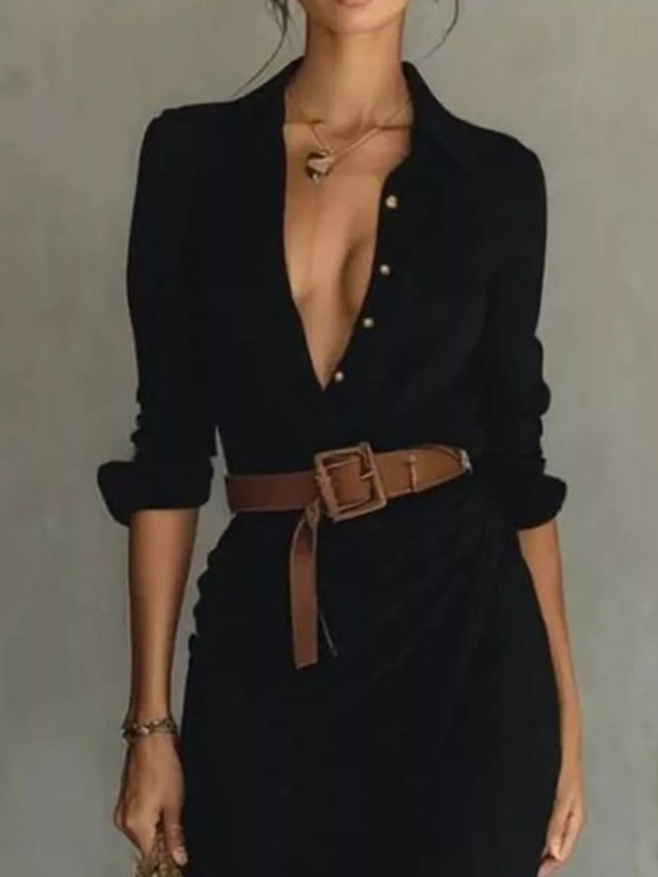 Person wearing a black dress with a deep neckline and brown belt against a gray background