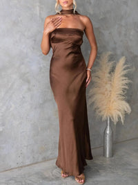 Woman wearing a brown halter neck gown against a gray concrete wall with a vase of pampas grass.