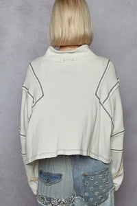 Person wearing a light-colored sweater with geometric patterns over a denim outfit on a gray background