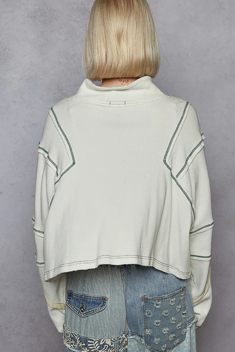 Person wearing a light-colored sweater with geometric patterns over a denim outfit on a gray background