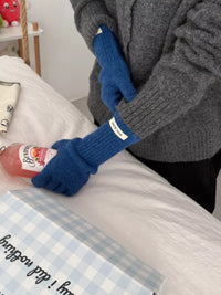 Person wearing blue gloves holding a bottle on a bed with a checkered blanket.