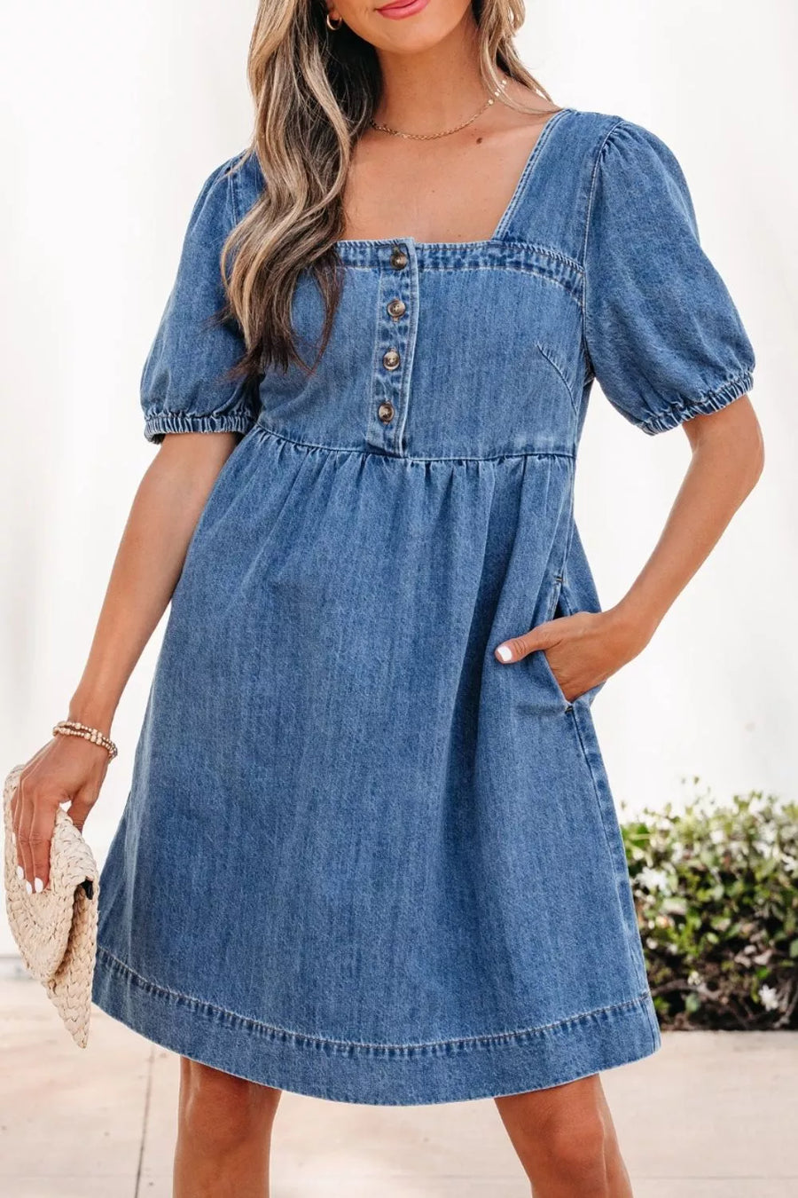 Woman wearing a blue denim dress with puff sleeves against a blurred outdoor background