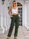 Woman wearing a white crop top and green cargo pants standing on a porch.