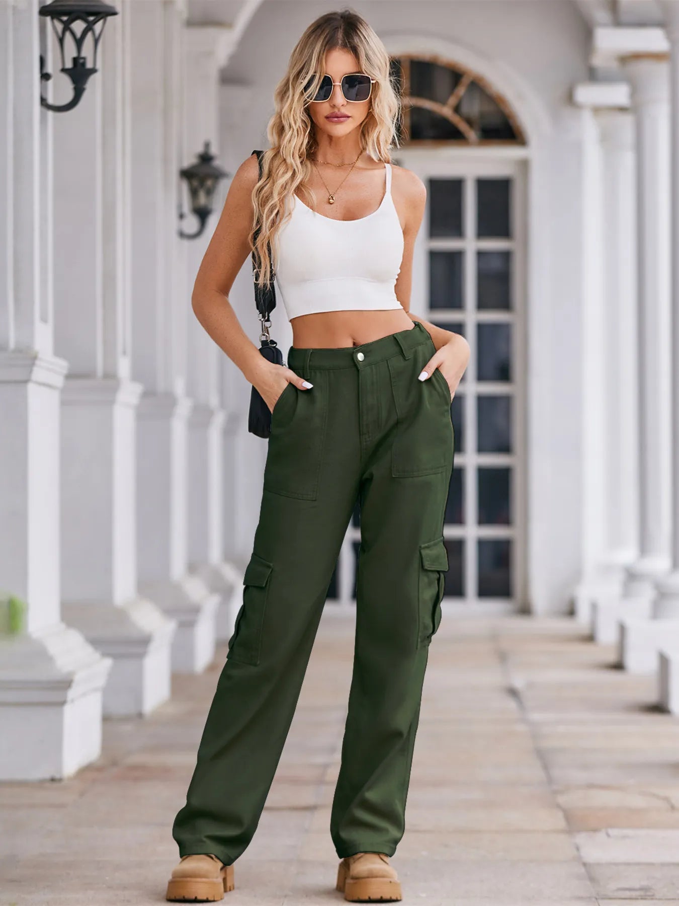 Woman wearing a white crop top and green cargo pants standing on a porch.
