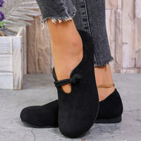 Black flat shoes worn with gray jeans on a stone pavement.