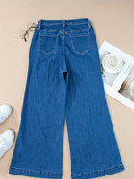 Blue jeans on a beige surface with white sneakers and a magazine.