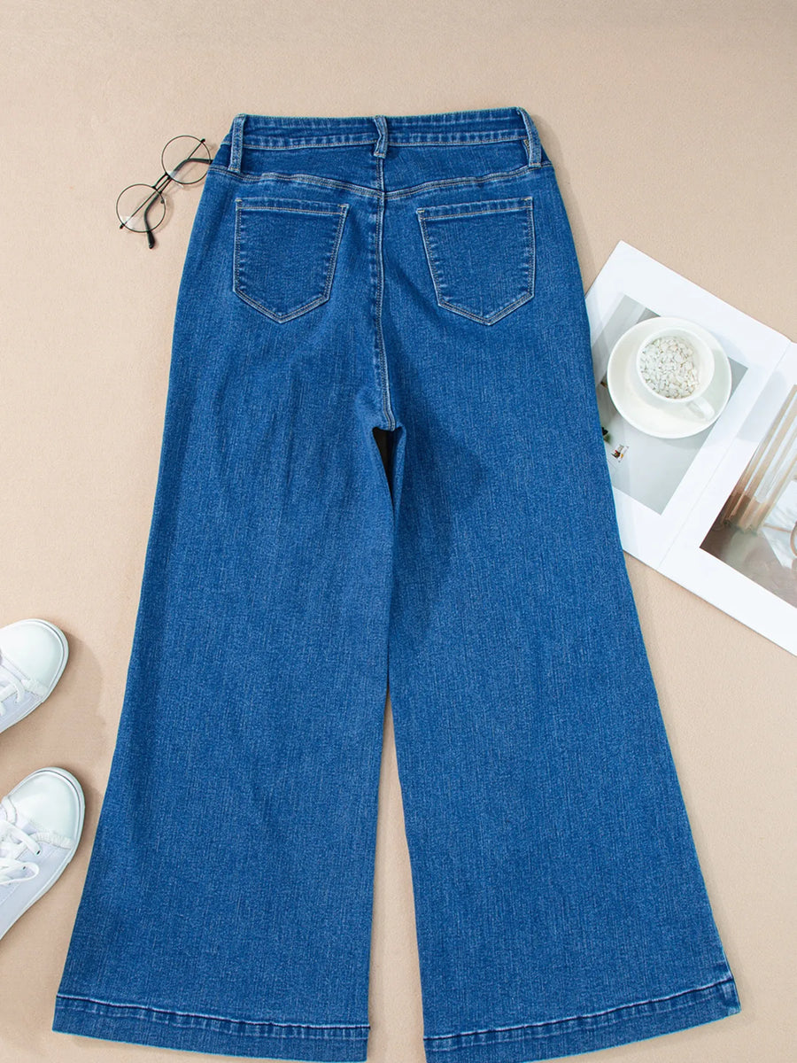 Blue jeans on a beige surface with white sneakers and a magazine.