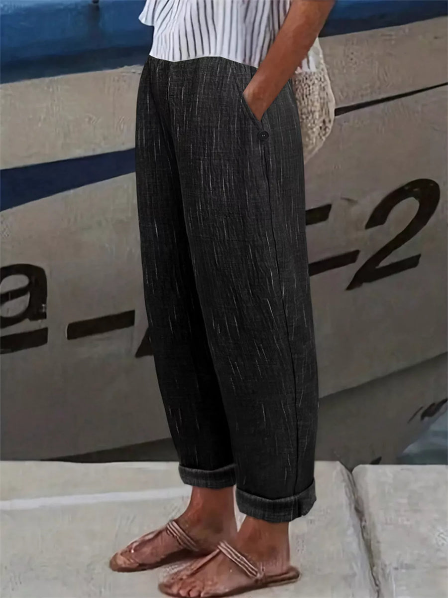A person wearing dark charcoal gray textured wide-leg trousers with rolled cuffs, paired with a white striped top and brown sandals, standing outdoors in front of a boat.