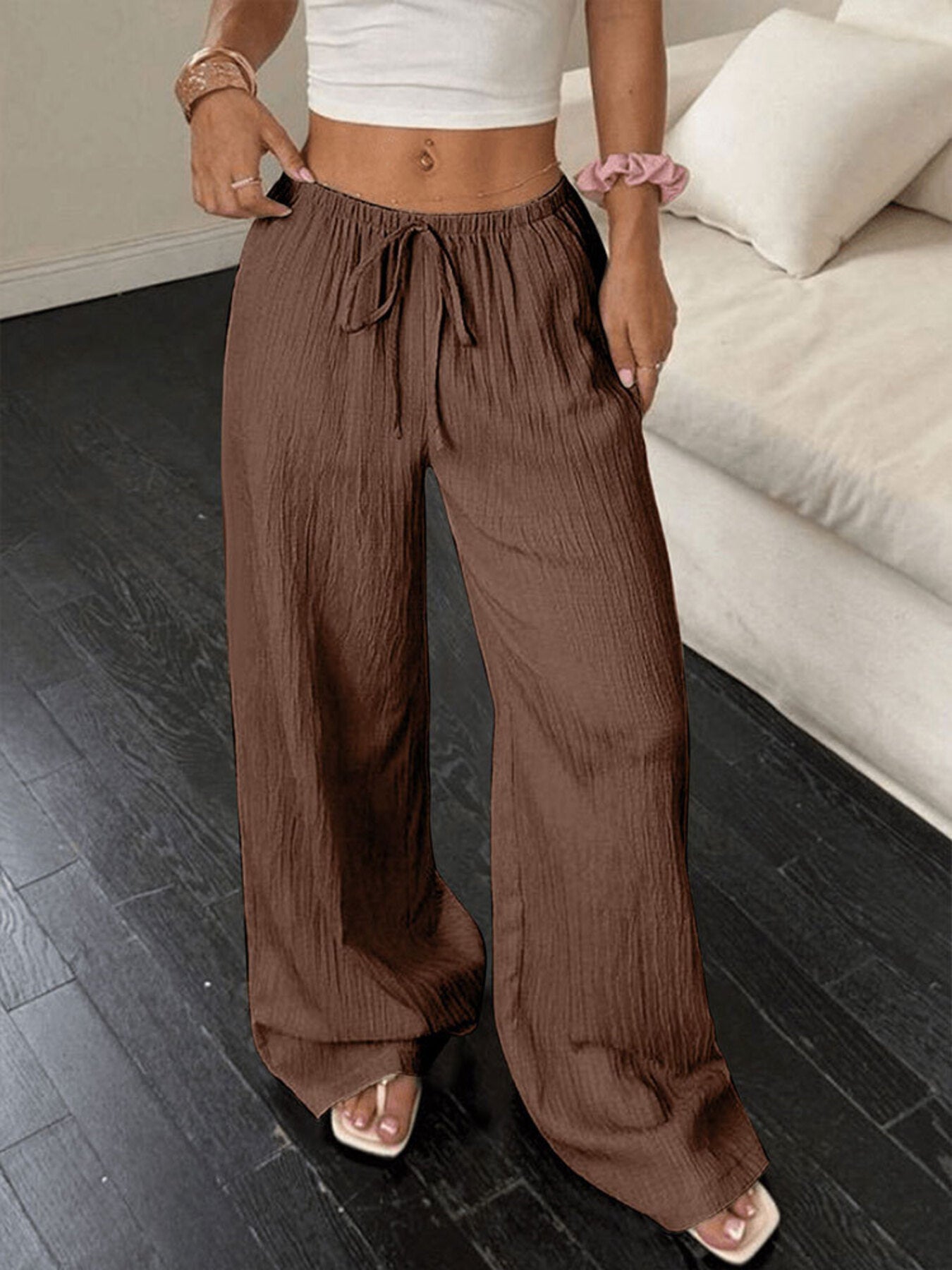 Person wearing brown wide-leg pants and a white top in a room with a couch.