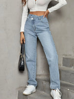 Person wearing a white cropped top and blue jeans standing against a gray wall.