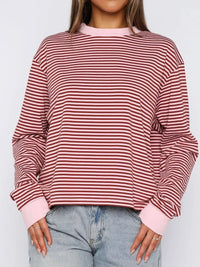 Person wearing a red and pink striped sweater with light blue jeans on a white background