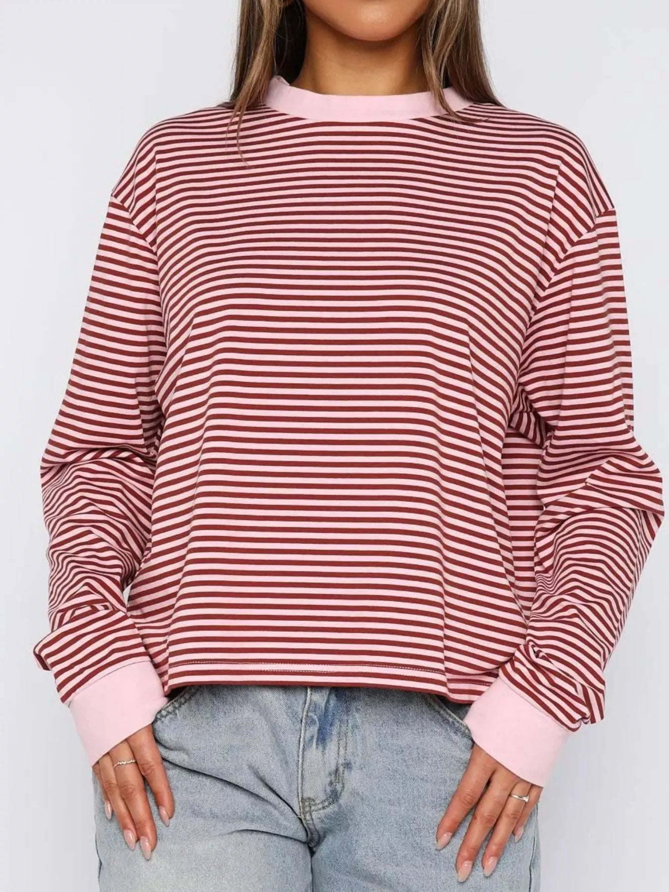 Person wearing a red and pink striped sweater with light blue jeans on a white background