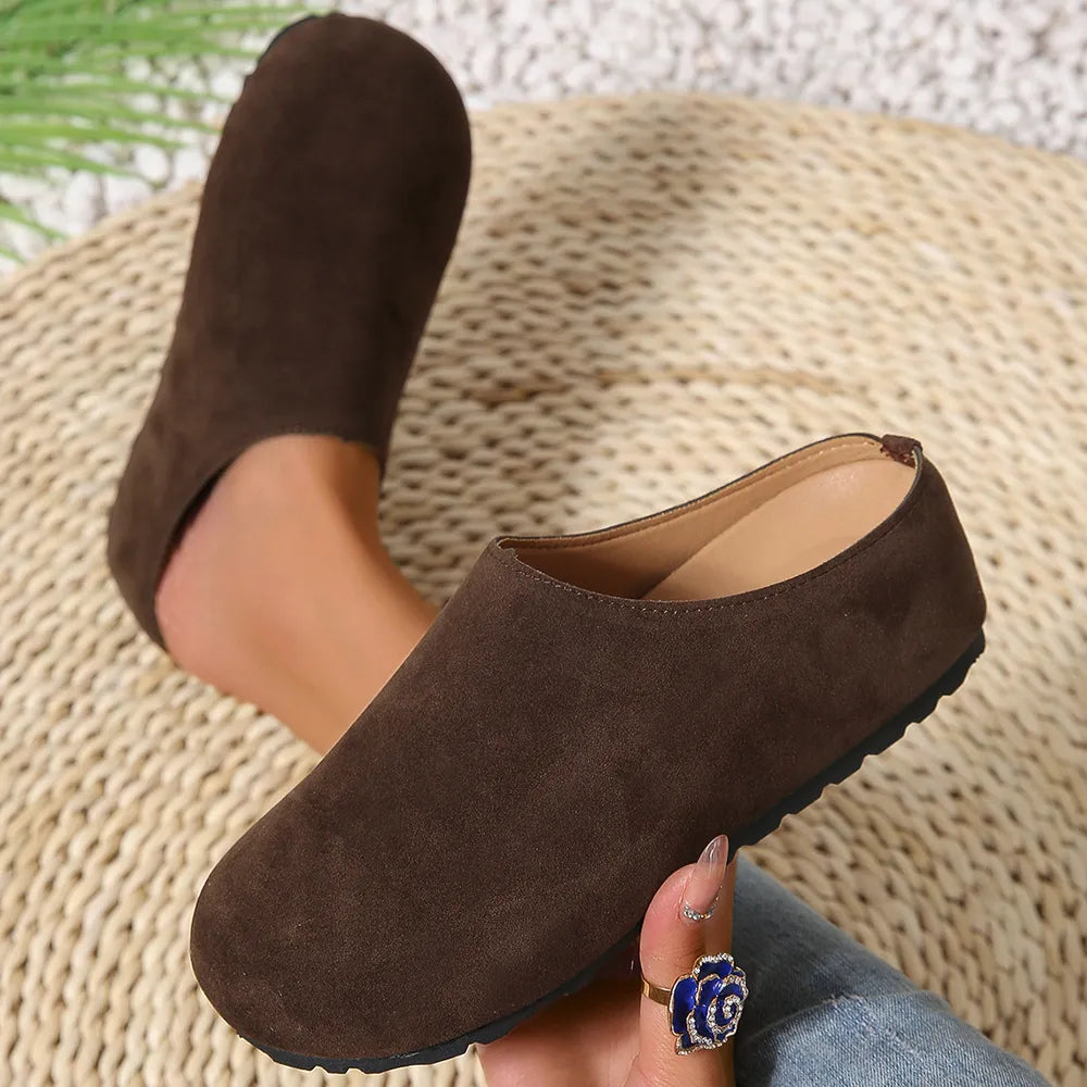 Brown suede clogs worn on a textured surface