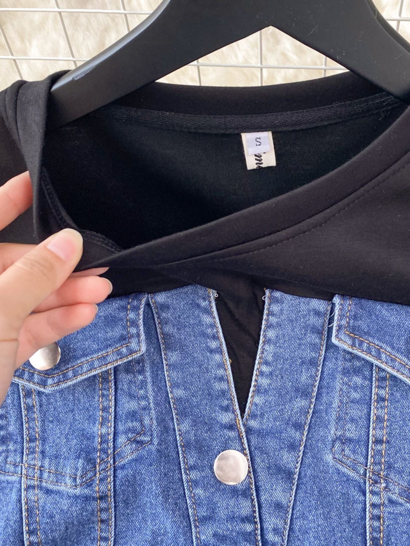 Black t-shirt on a hanger with a blue denim jacket in the foreground