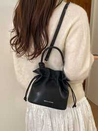 Person wearing a black drawstring bag over their shoulder with a neutral background