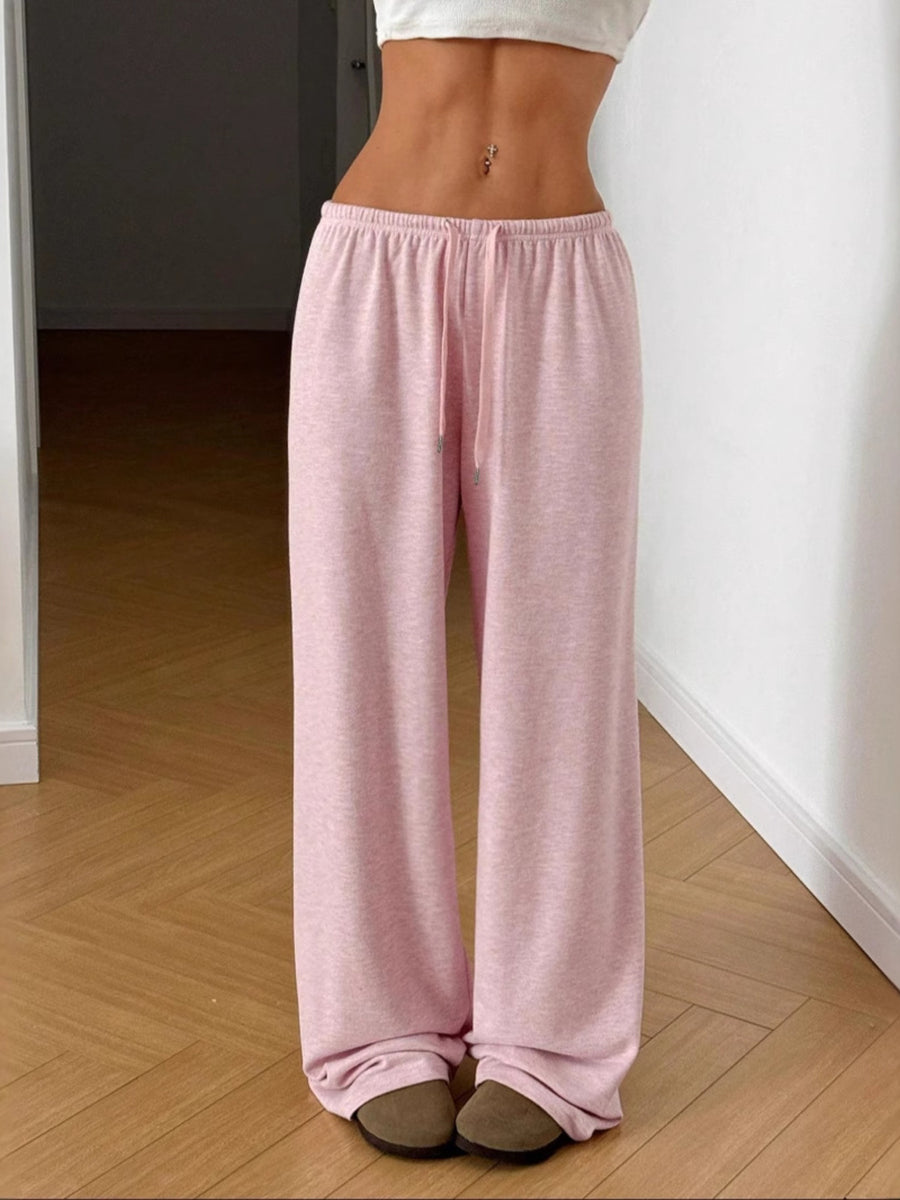 Person wearing pink pajama pants standing on a wooden floor.