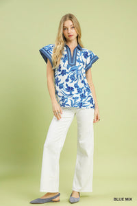 Woman wearing a blue and white floral blouse with white pants on a light green background