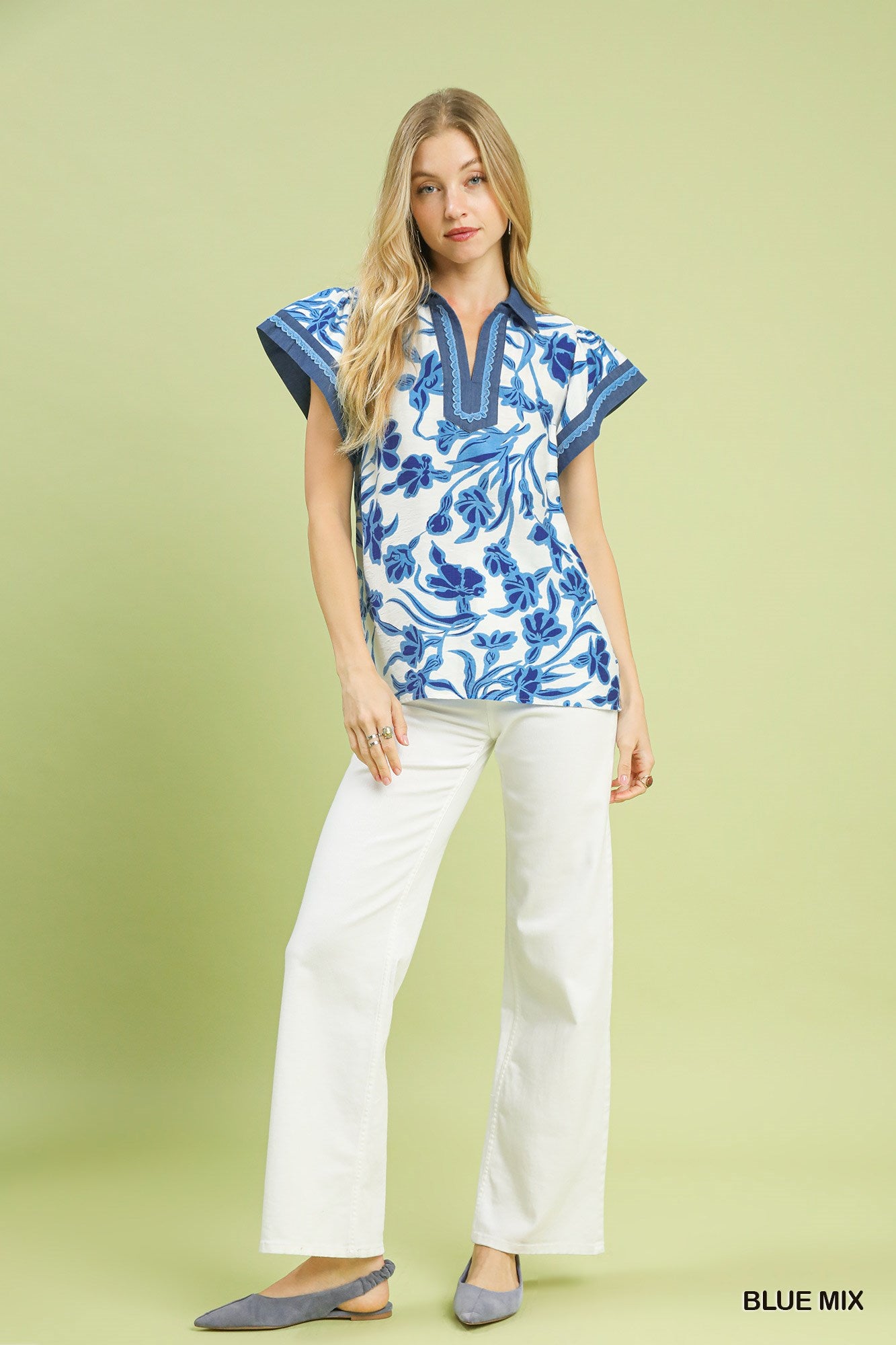Woman wearing a blue and white floral blouse with white pants on a light green background