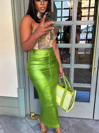 Woman in a green skirt and patterned top holding a matching bag, taking a mirror selfie.