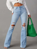 Person wearing light blue ripped jeans and a white cropped top, holding a green bag on a gray background