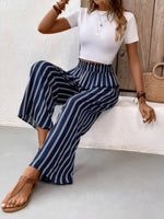 Woman wearing a white top and blue striped pants sitting on a bench.