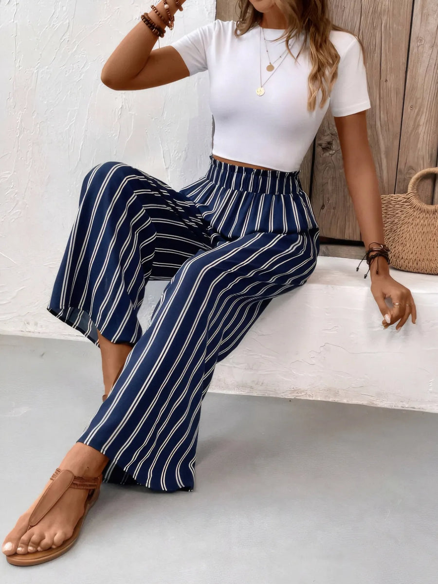 Woman wearing a white top and blue striped pants sitting on a bench.