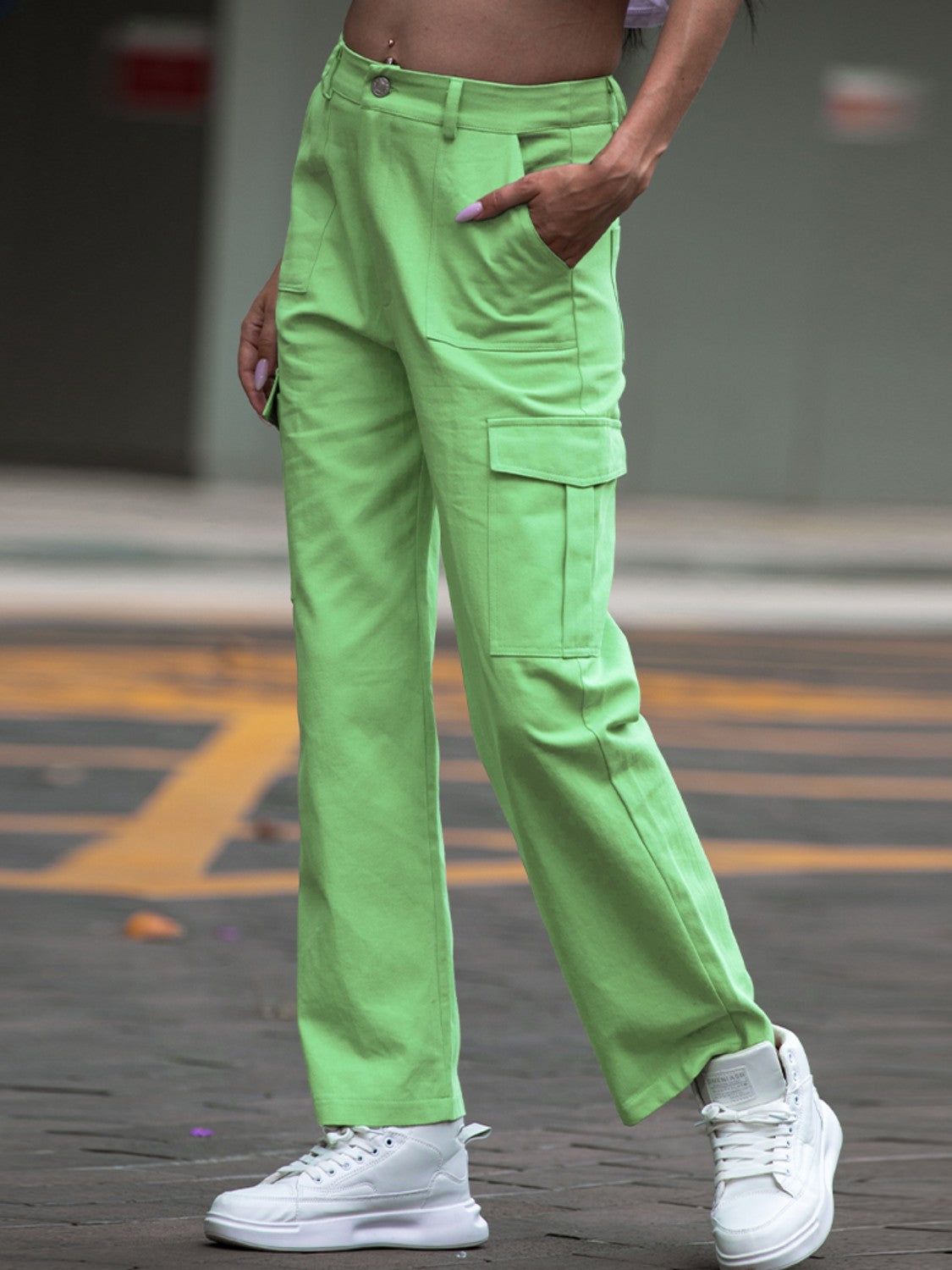 Person wearing bright green cargo pants and white sneakers on a blurred street background