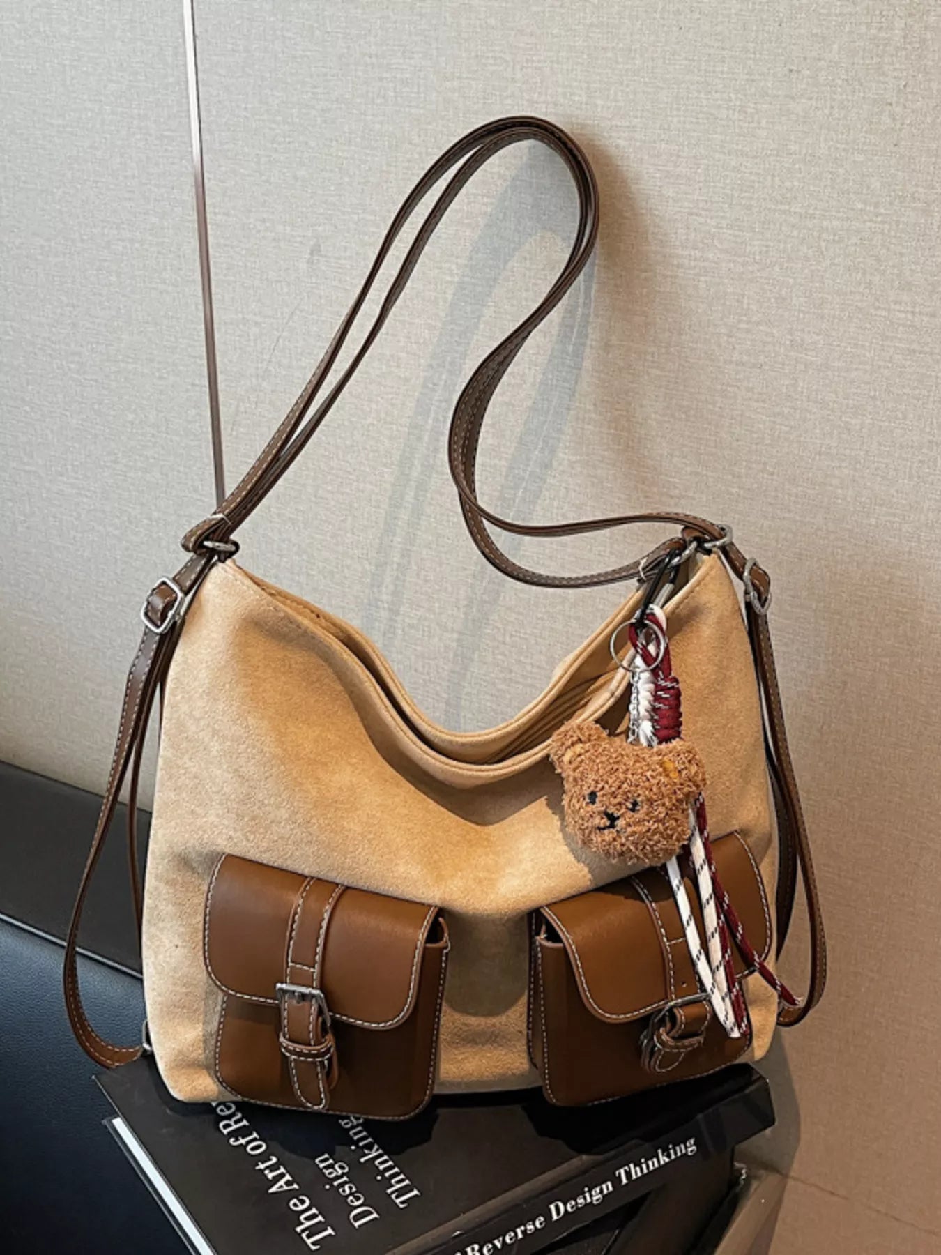 Brown handbag with a teddy bear keychain on a reflective surface