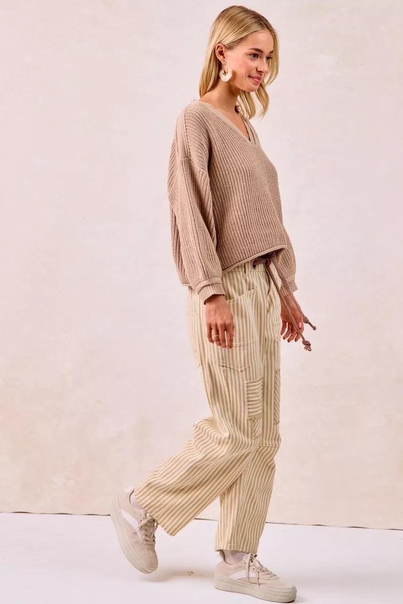 Woman wearing a beige sweater and striped pants against a plain background
