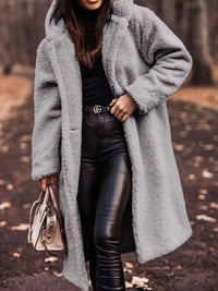 Person wearing a long gray coat with a blurred natural background