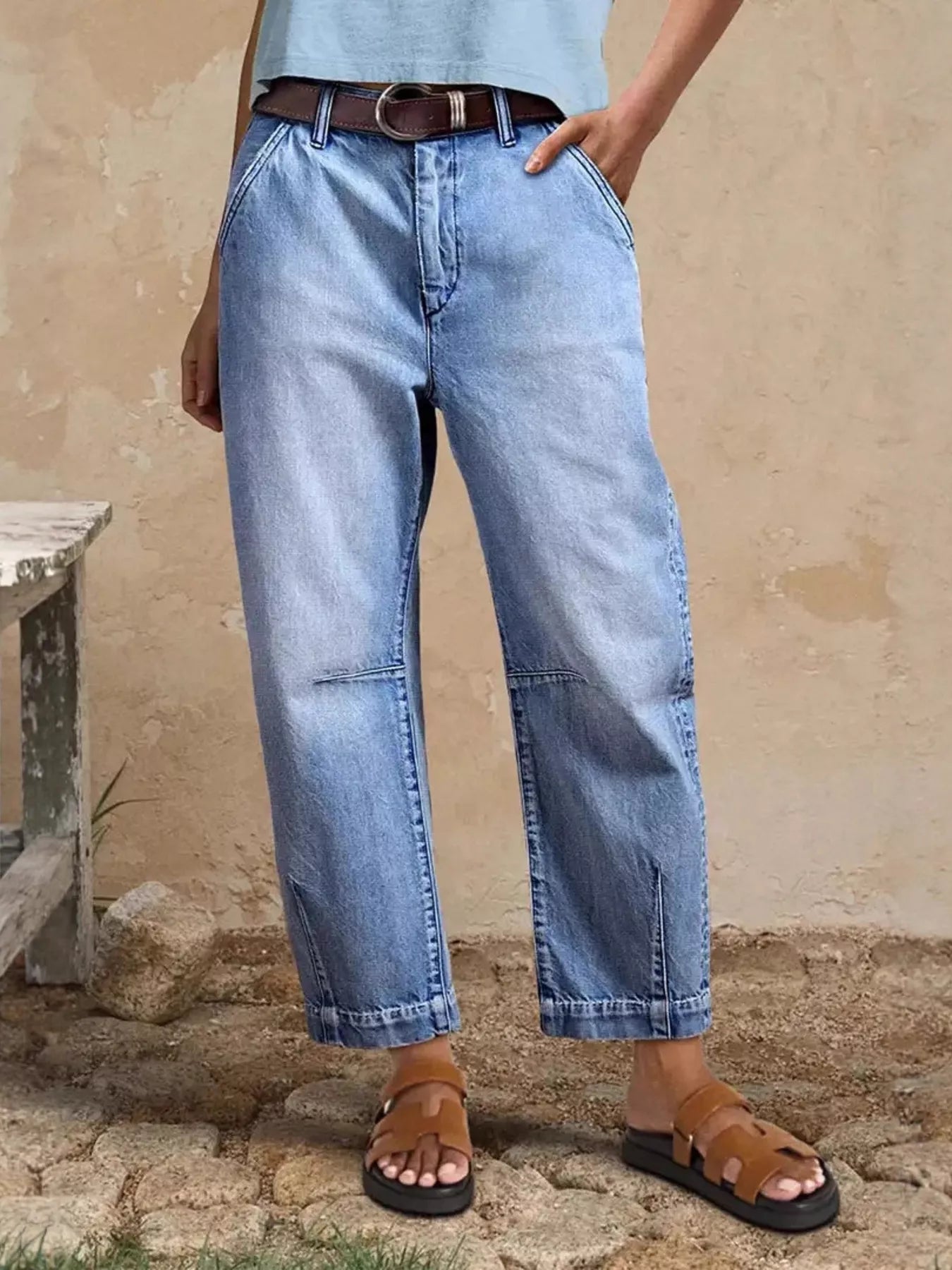 Person wearing blue jeans and brown sandals against a beige wall.