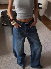 Person wearing blue jeans and a gray top in a room with a rug and furniture.