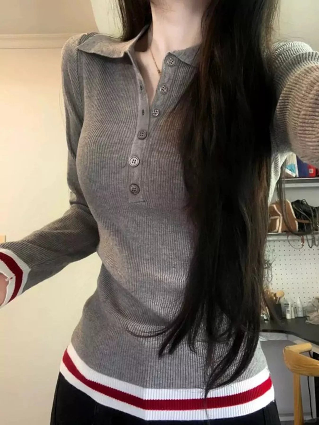 Person wearing a gray sweater with red and white accents in an indoor setting