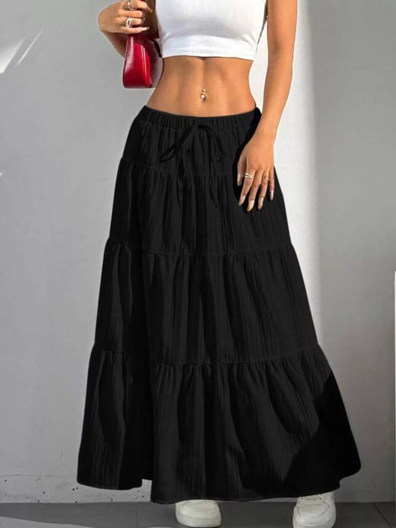 Person wearing a black tiered skirt with a white top against a gray background