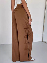 Brown wide-leg pants with tie details worn by a person on a white background