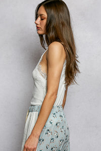 Woman wearing a white lace top and light blue floral skirt against a gray background