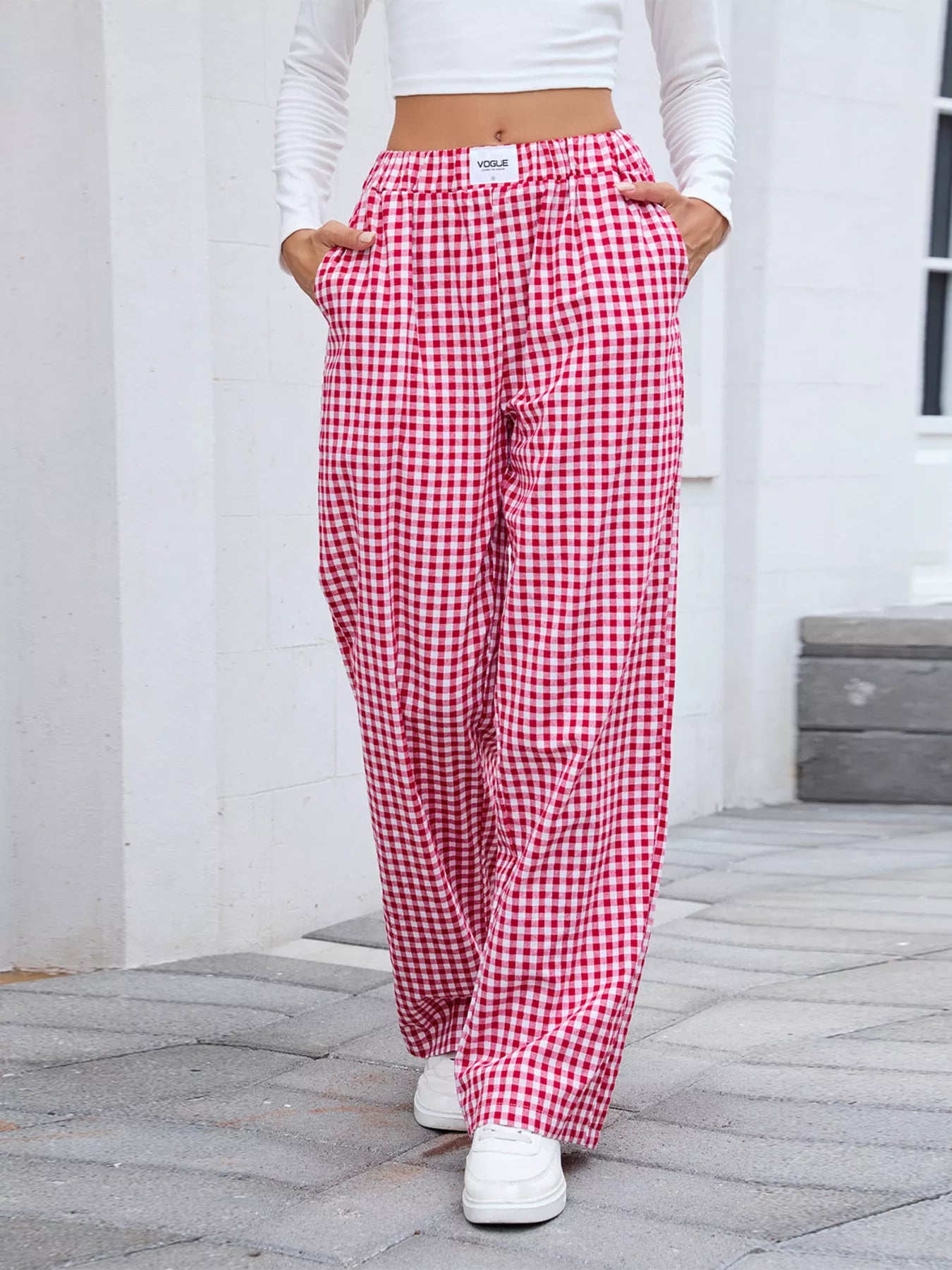 Person wearing red and white checkered pants with a white top and white sneakers on a stone path.