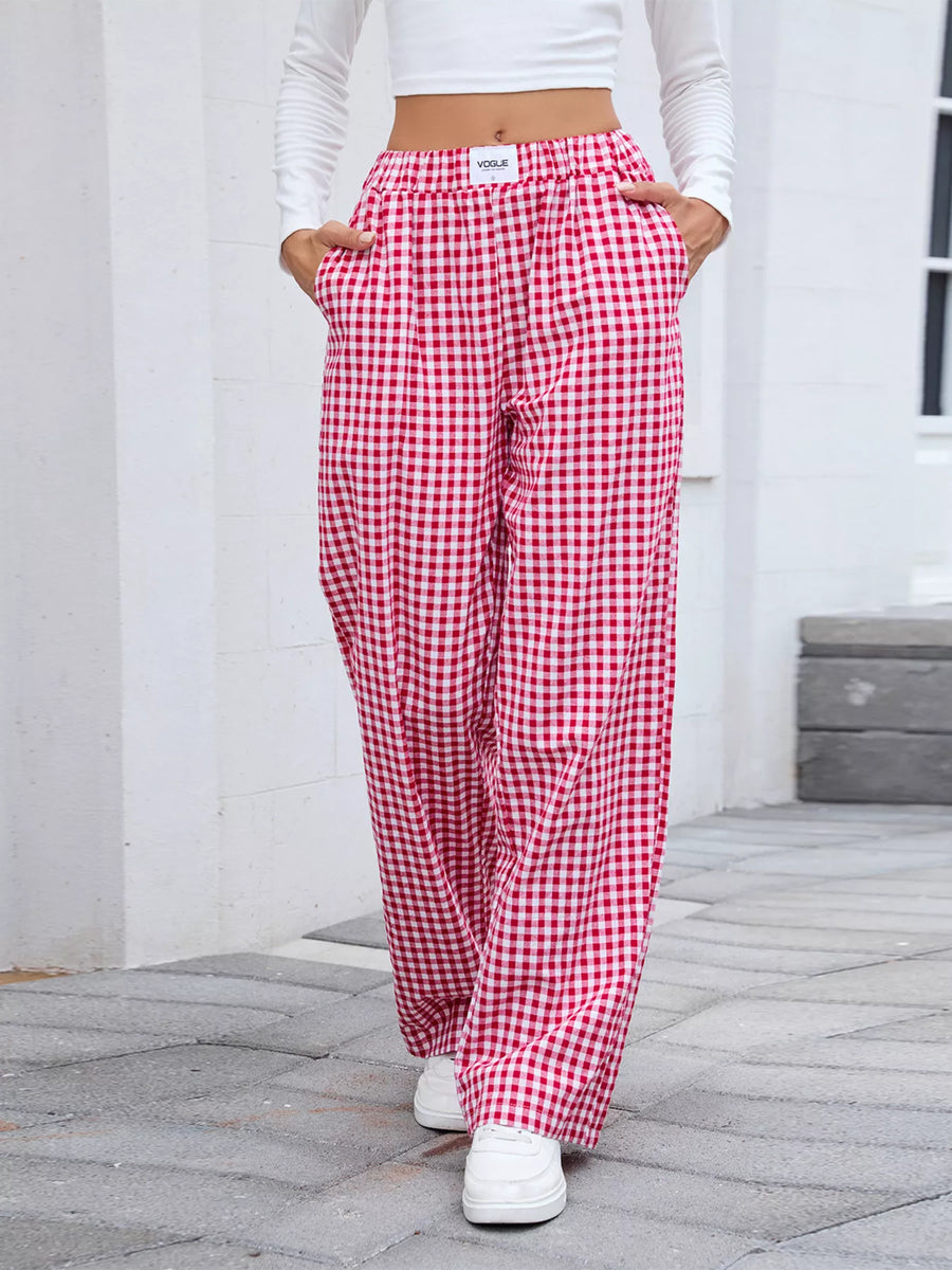 Person wearing red and white checkered pants with a white top and white sneakers on a stone path.