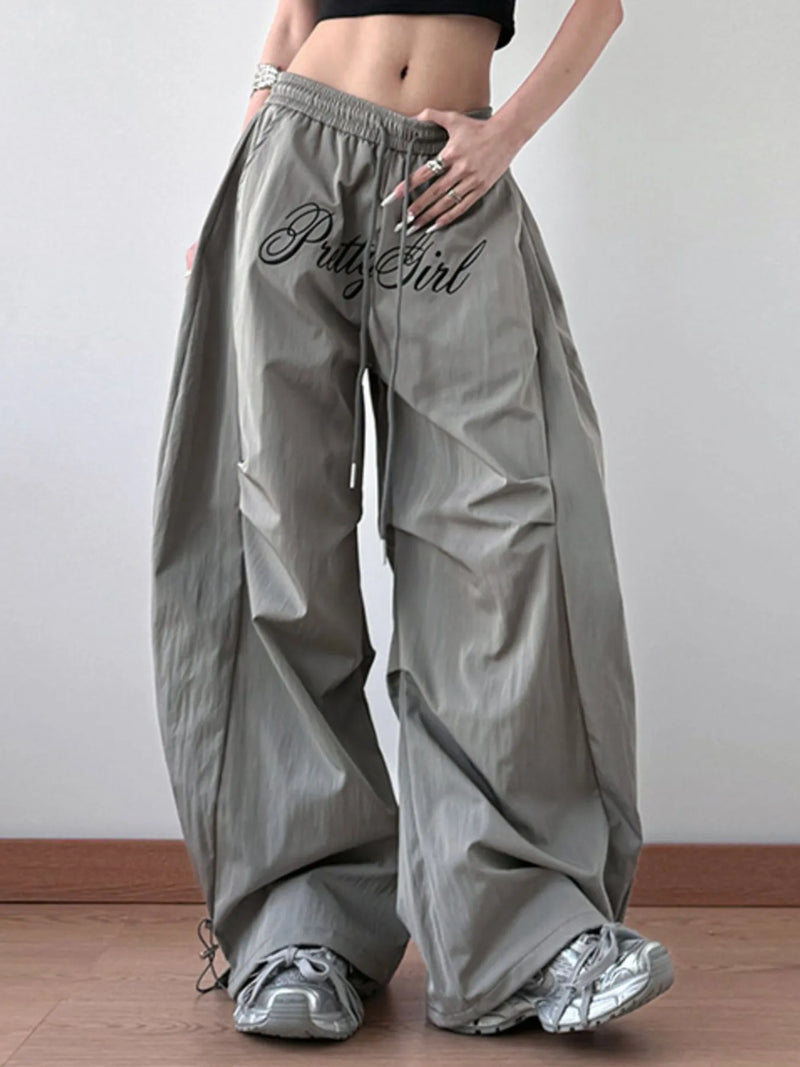 Person wearing gray wide-leg pants with 'B*tch Girl' text, standing against a plain background.