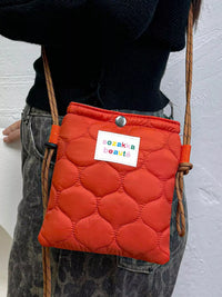 Person wearing an orange quilted bag with a visible brand label on a plain background