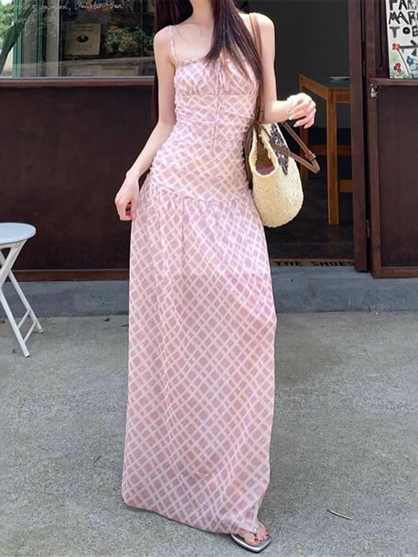 Woman wearing a pink lace dress holding a beige handbag on a sidewalk.