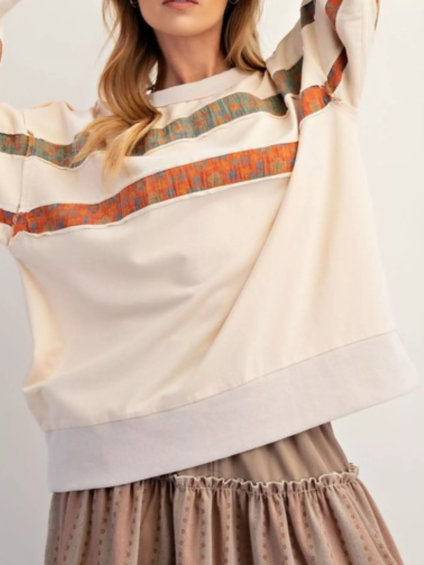 Woman wearing a cream-colored top with patterned trim and a brown skirt on a white background