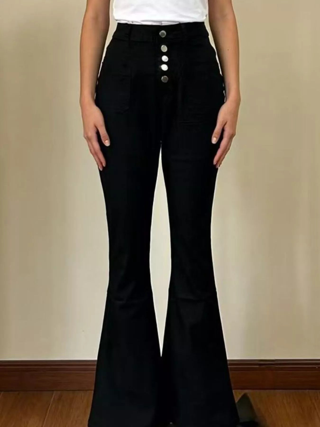 Black bell-bottom pants with silver buttons worn by a person on a beige background