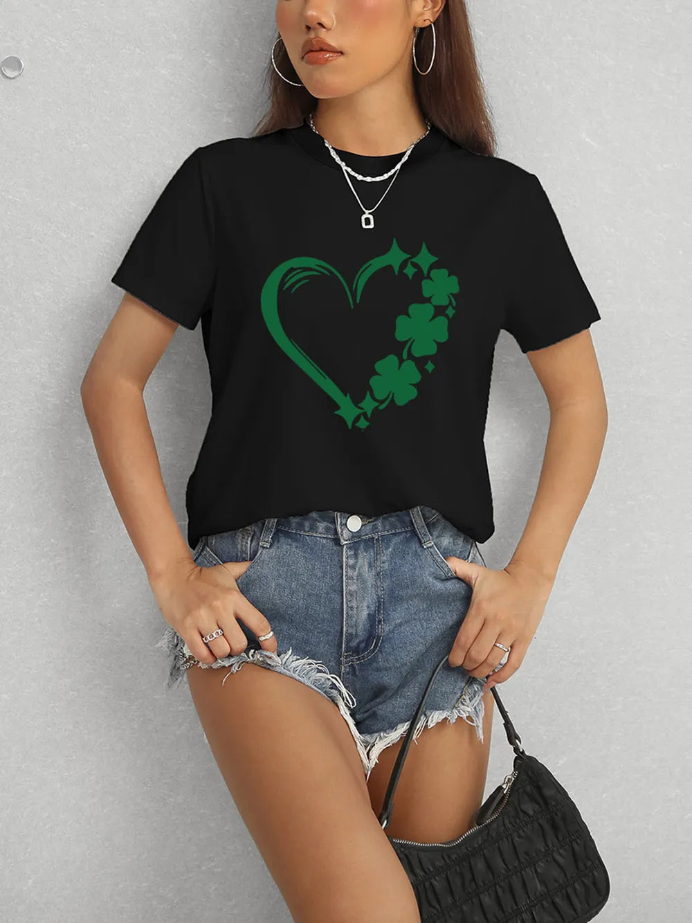 Person wearing a black t-shirt with a green heart and shamrock design, denim shorts, and carrying a black handbag.