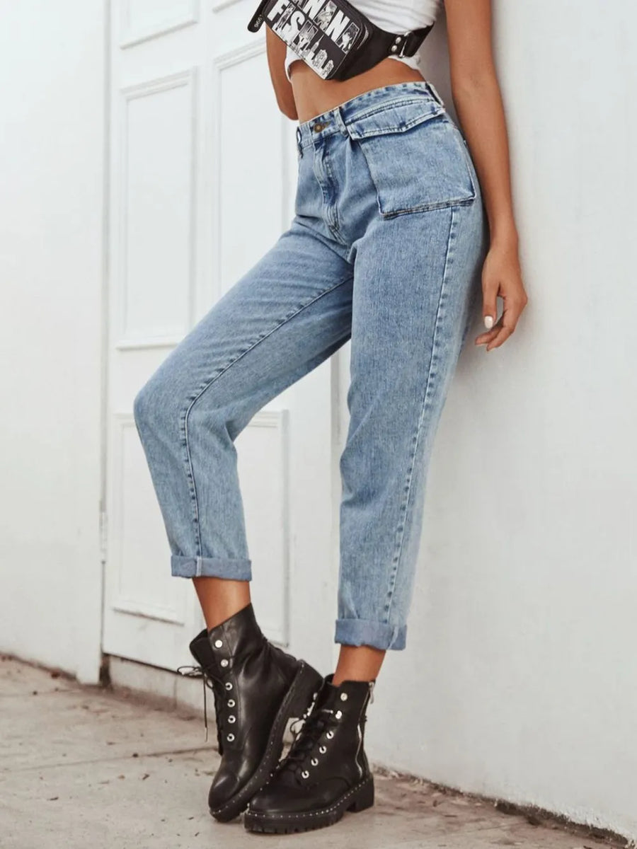 Person wearing blue jeans and black combat boots against a white wall.