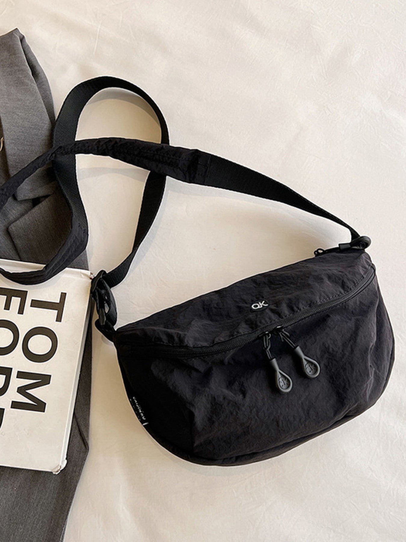 Black waist bag on a light gray surface with a book and gray pants.