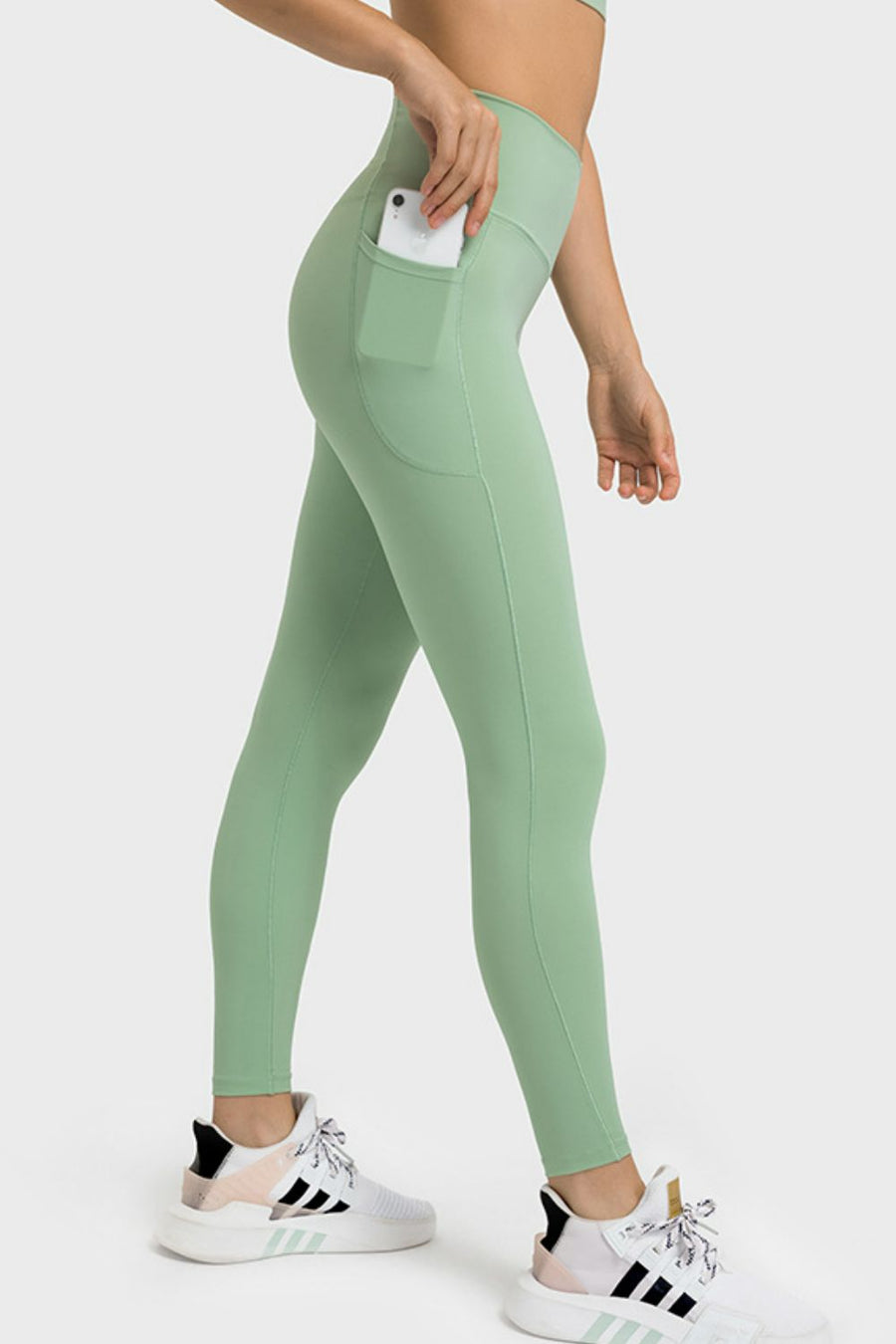 Person wearing green leggings with a pocket, standing on a white background