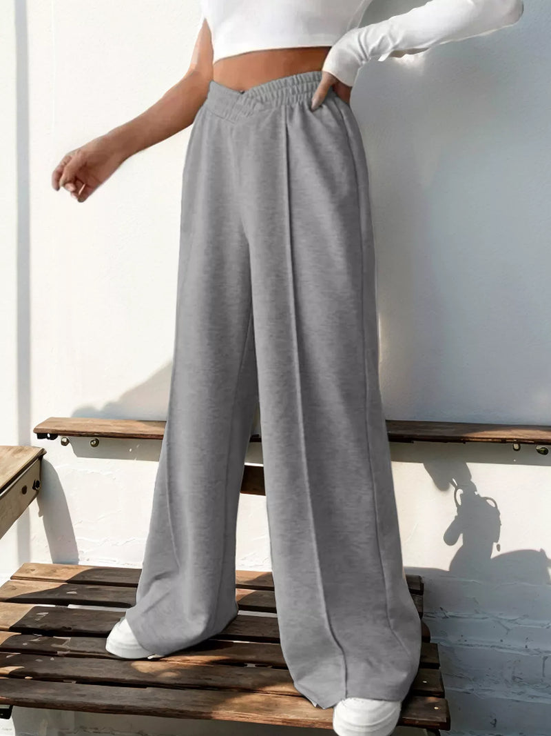 Person wearing gray sweatpants and a white top sitting on a wooden bench.