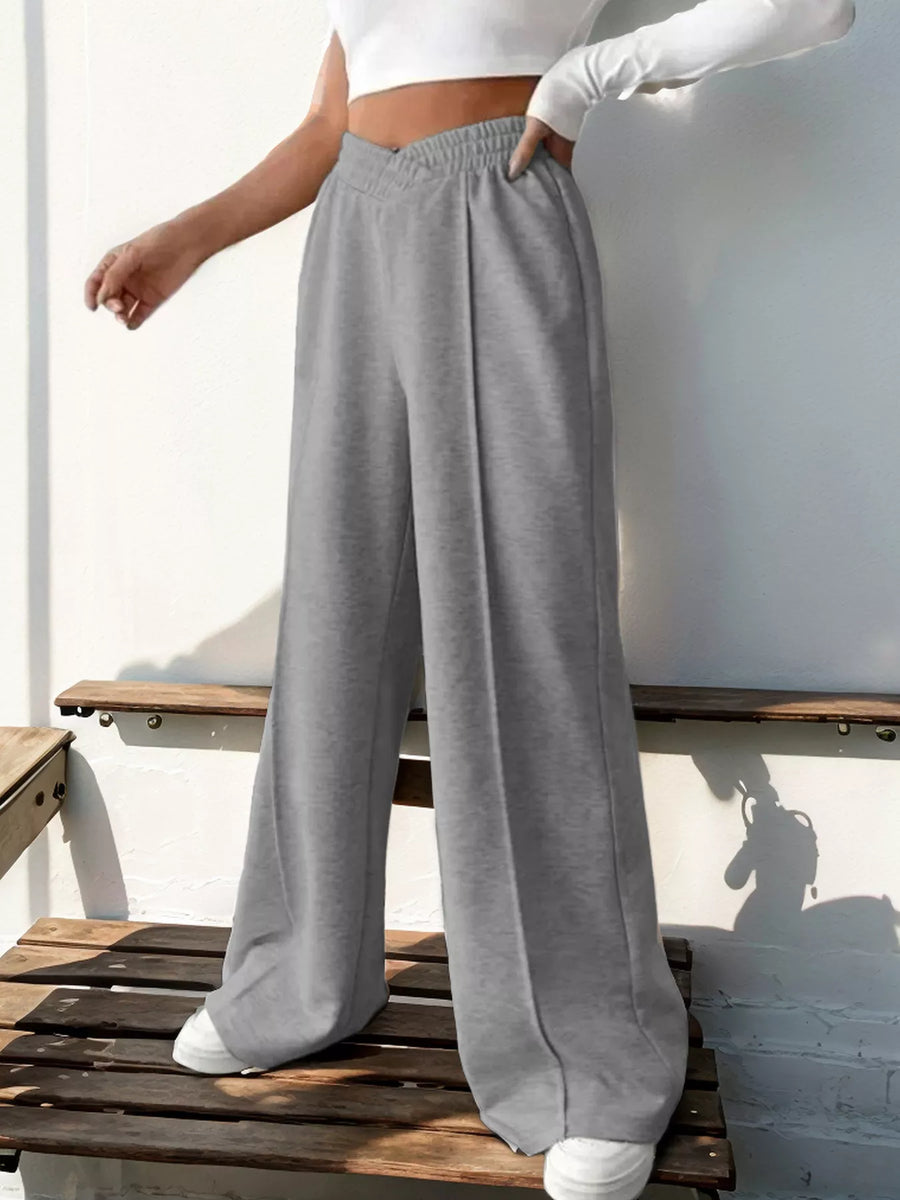 Person wearing gray sweatpants and a white top sitting on a wooden bench.