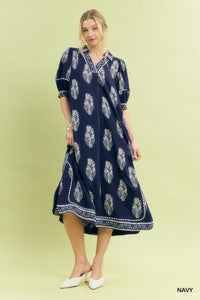 Woman wearing a navy dress with white floral pattern on a light green background